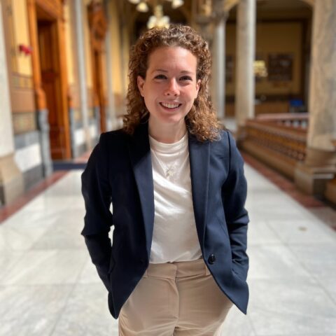 Casey Smith in a blue blazer and white shirt with beige slacks in a corridor that looks like a capitol building.