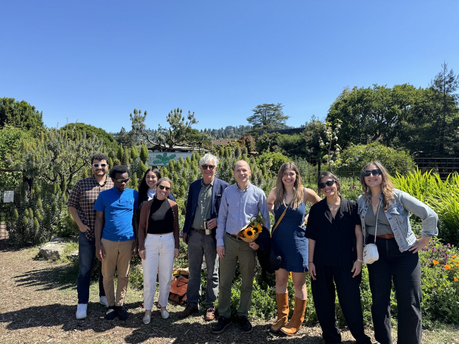 A group of people stand near a garden. they are students and professors.