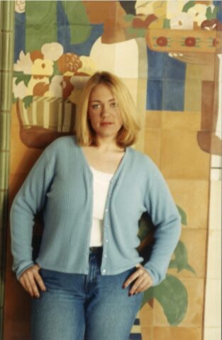 Smith in college, wearing blue jeans and a blue cardigan. Her hands are on her hips and she's looking directly into the camera. 