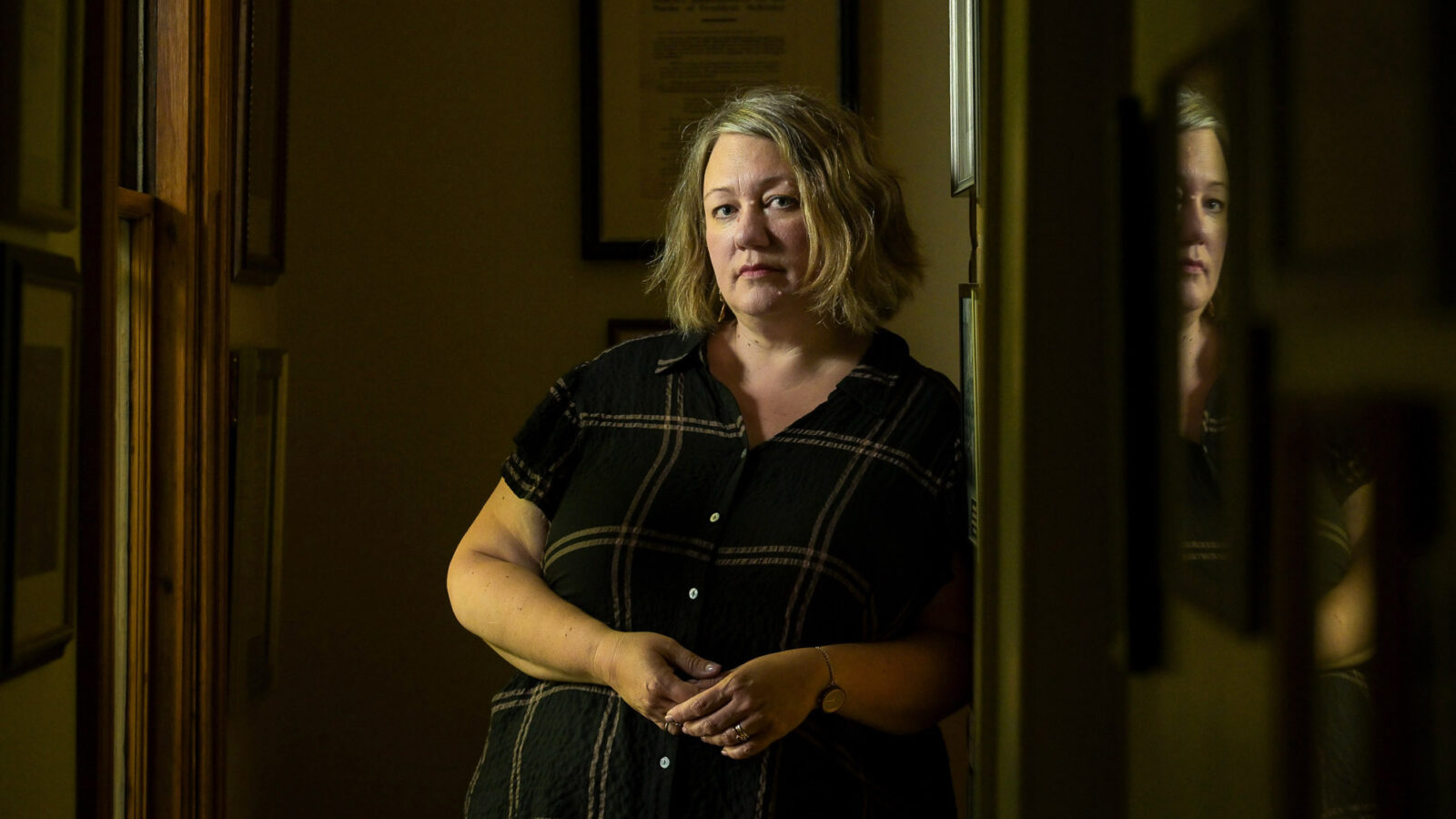 Joselyn Smith, a white woman with blonde hair, leans against the wall looking directly into the camera.