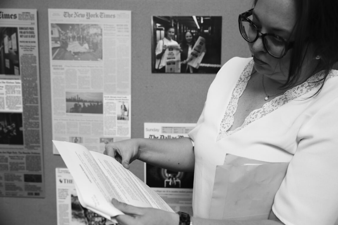 Katey Rusch looks at some documents in the offices of the Investigative Reporting Program. There are newspapers on bulletin boards behind her. The photo is in black and white.