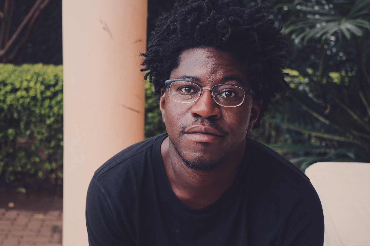 Image of an African American man wearing glasses and a black tshirt looking at the camera.