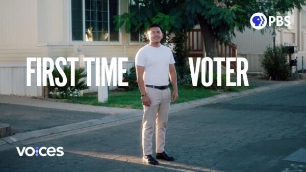 Man standing in a white t-shirt and beige slacks in front of a neat house with the words First Time Voter and Voces on the image.