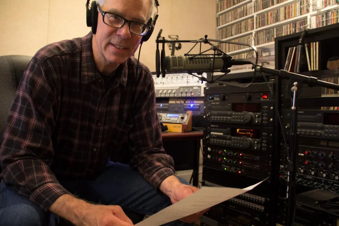 Image of a man wearing audio headphones holding a paper script in a studio.