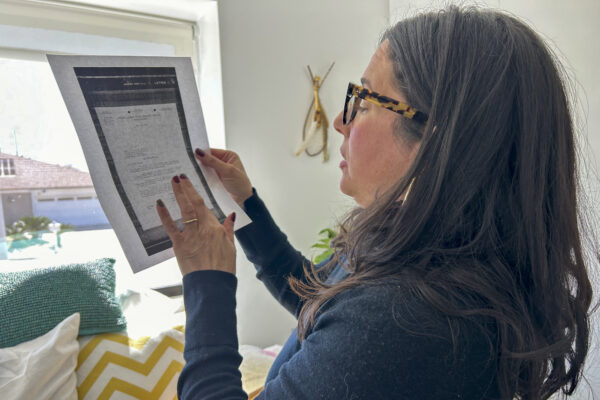 Stact Cordova, wearing a blue top and glasses, holds up and examines a printed sheet of paper. 