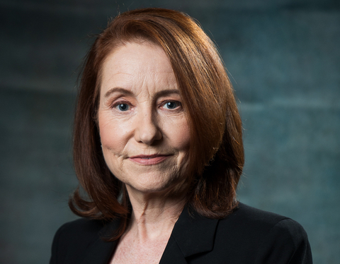 Woman with dark red hair in a bob wearing a black elegant suit smiling.