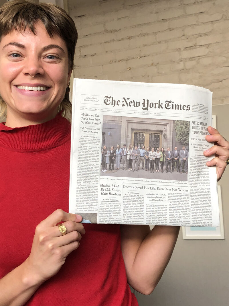 A woman wearing a bright red sweater with short brown hair holds up a print copy of the New York Times with her byline.