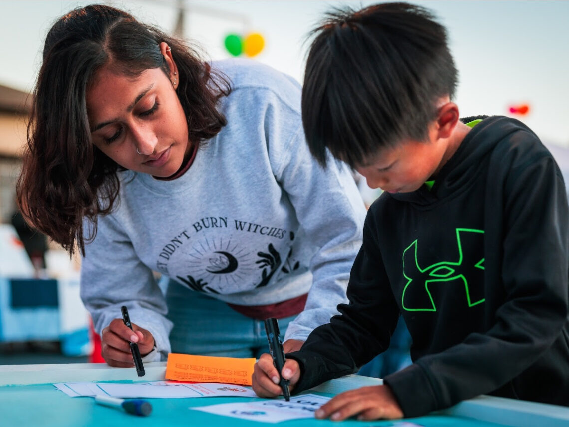 A young woman and young boy with dark hair draw intently on a table.