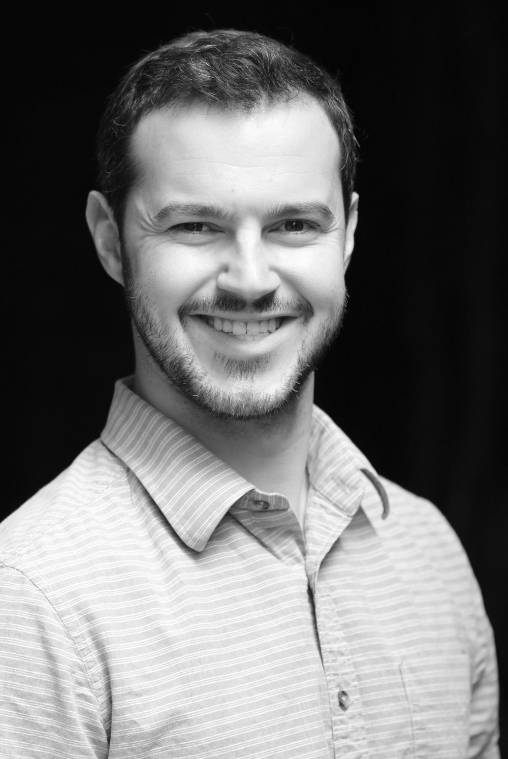 black and white photo of a man with a short goatee who is smiling. The photo is of Peter Bittner. It's a headshot.