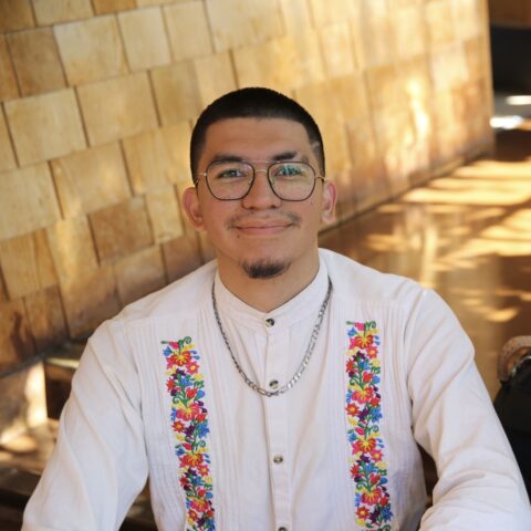 Student sitting in the hallway at North Gate Hall in a white guerabara shirt. 