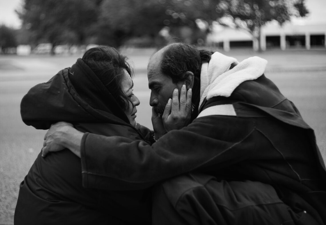 Black and white of a woman and a man crouched down and holding eachother's faces closely.