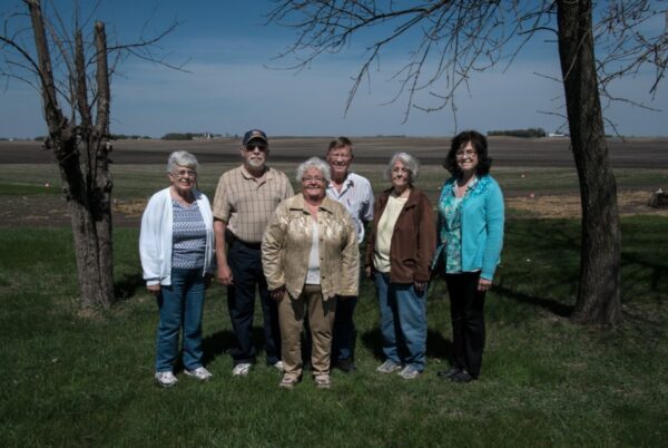 Two men and four women stand in front a field, smiling at the camera.