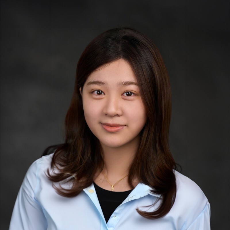 A young woman with long dark hair wearing a white button down over a black tshirt smiles in front of a black background.