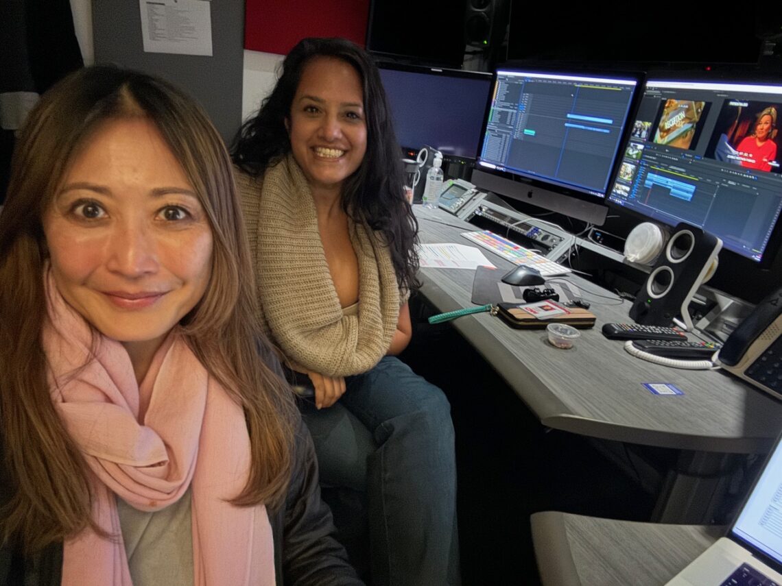 Two women sitting next to oneanother in an editing bay smiling.