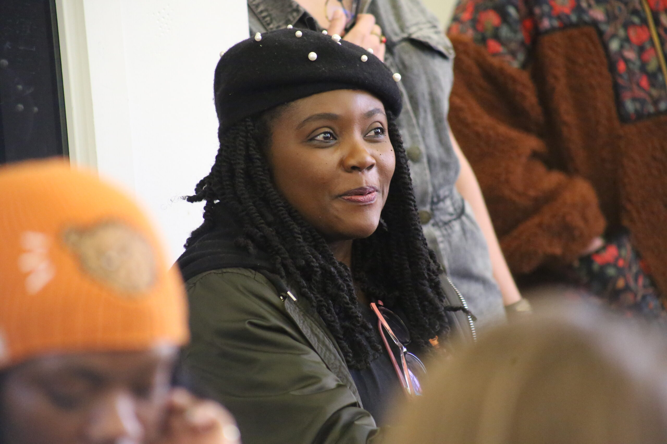 A young woman in a cap sits among others in an audience. Focus is on her face and she's slightly smiling.