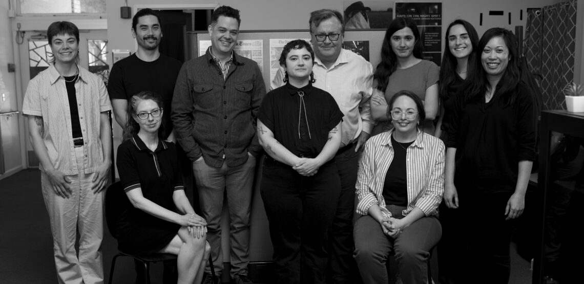 Black and white group portrait of the reporters and teachers at the IRP standing and sitting in a newsroom.
