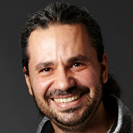 Close up headshot of a man with dark brown hair and a beard and mustache smiling brightly.