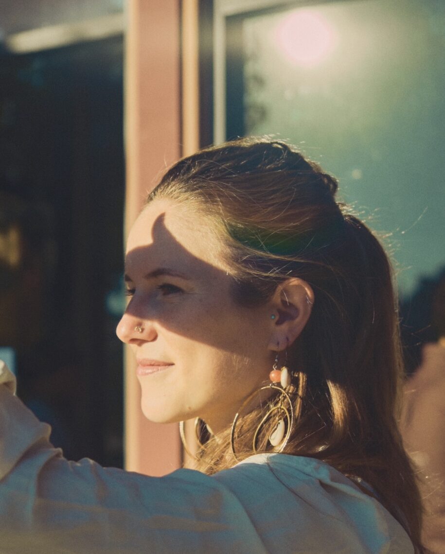 A young woman with dark blonde hair in a pony tail faces the sun with her hand to shield her face.