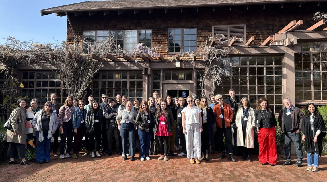 A large group of people standing in front of a brown shingled building on a brick courtyard.