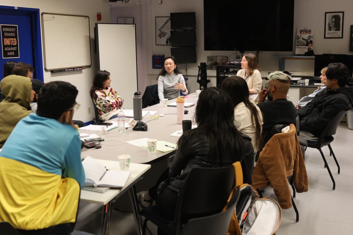 A group of journalism graduate students sit around a long table listening to a woman speak.