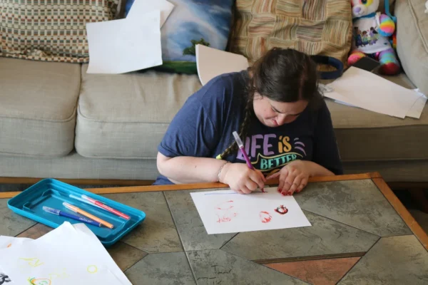 Rachel Tung sits at the coffee table drawing on white paper with markers.