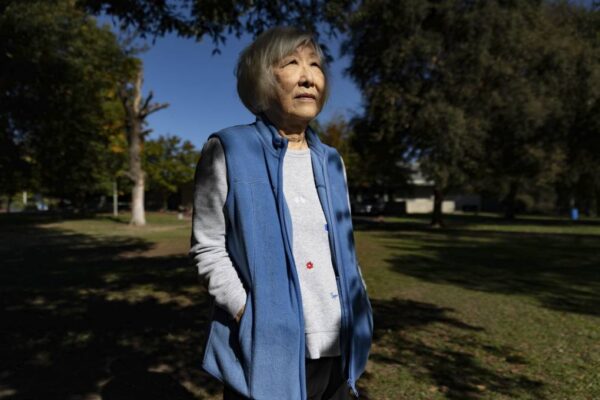 Frances Kakugawa stands in an outdoor green space wearing a white shirt and blue fleece vest. 