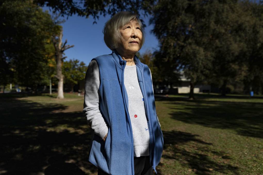 Frances Kakugawa stands in an outdoor green space wearing a white shirt and blue fleece vest.