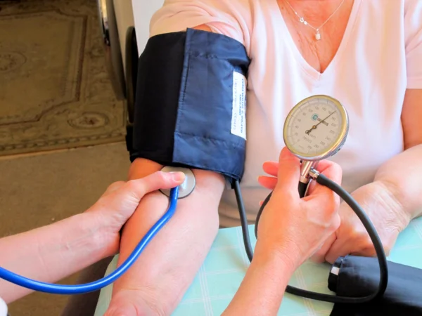 Photo of a white woman's arm with a blood pressure cuff being held by a medical provider.