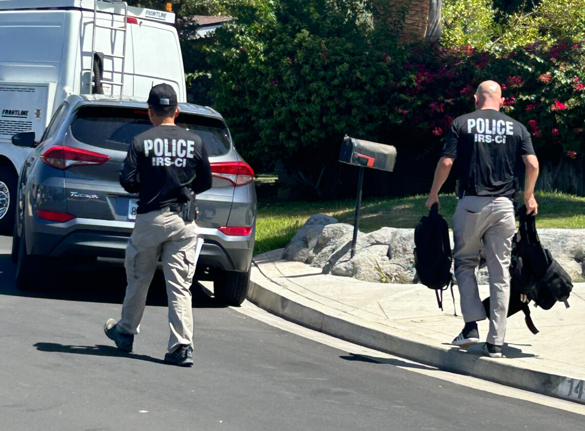 Two federal agents walking towards a house.