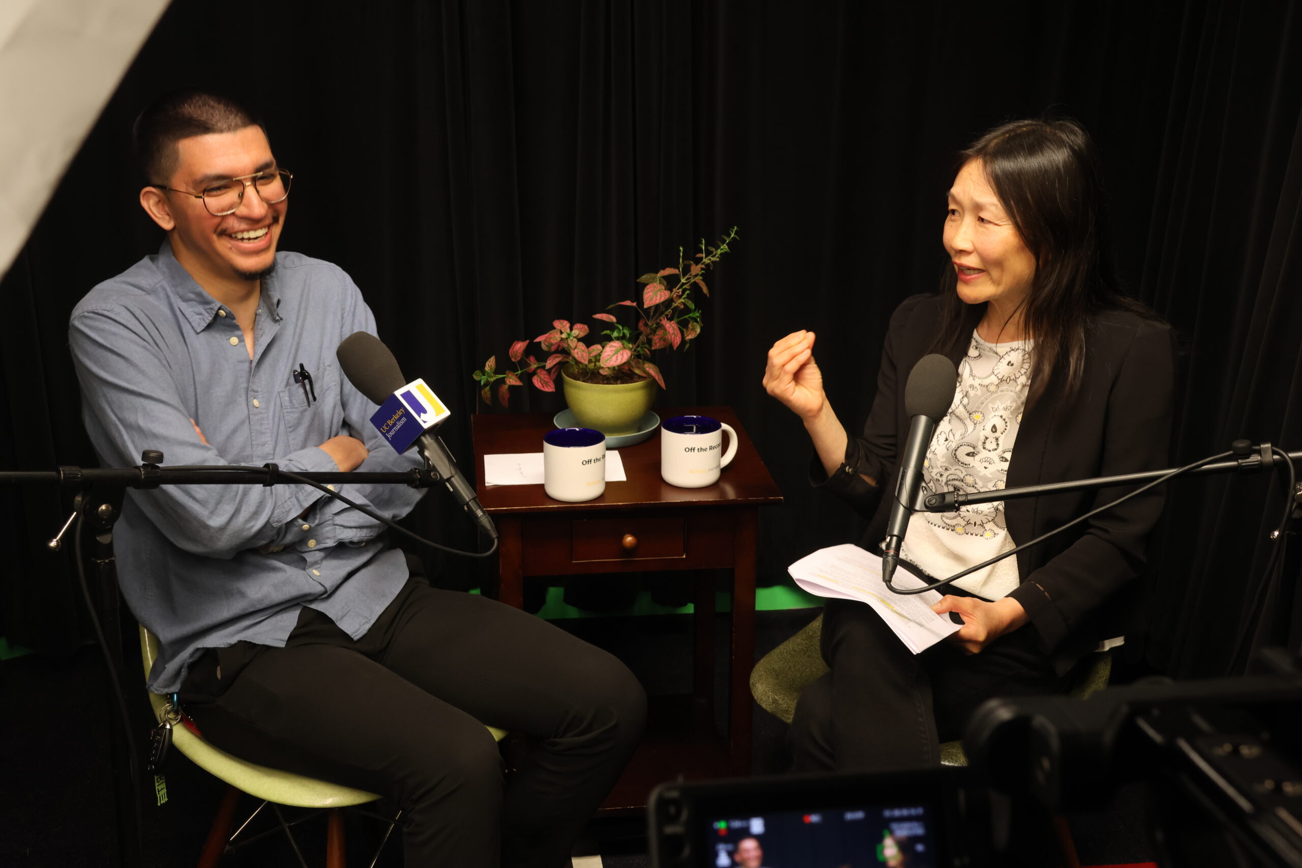 Two people doing an interview facing each other in chairs in a dark studio.
