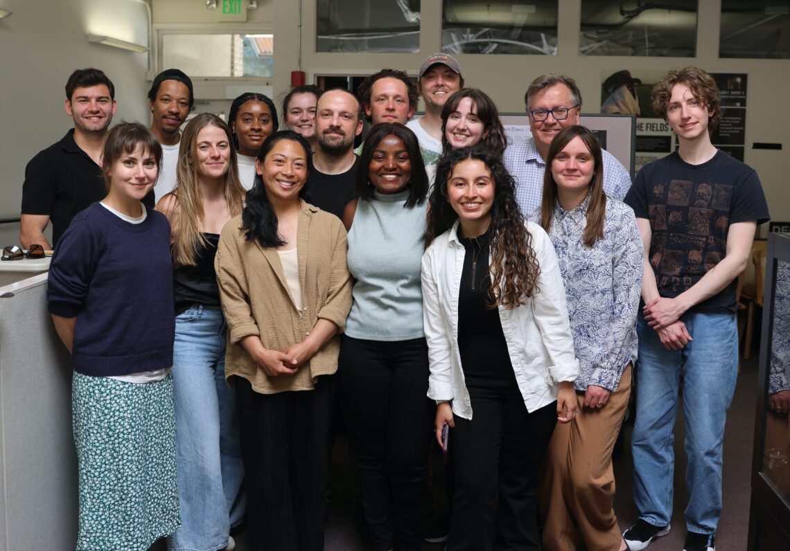 Large group of graduate students stands close together with their professor in the newsroom of the IRP.