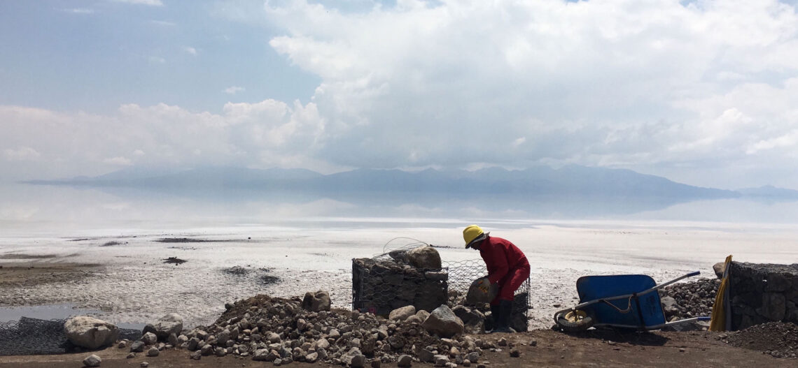 A person bent over rocks on a beach working with clouds in the background.
