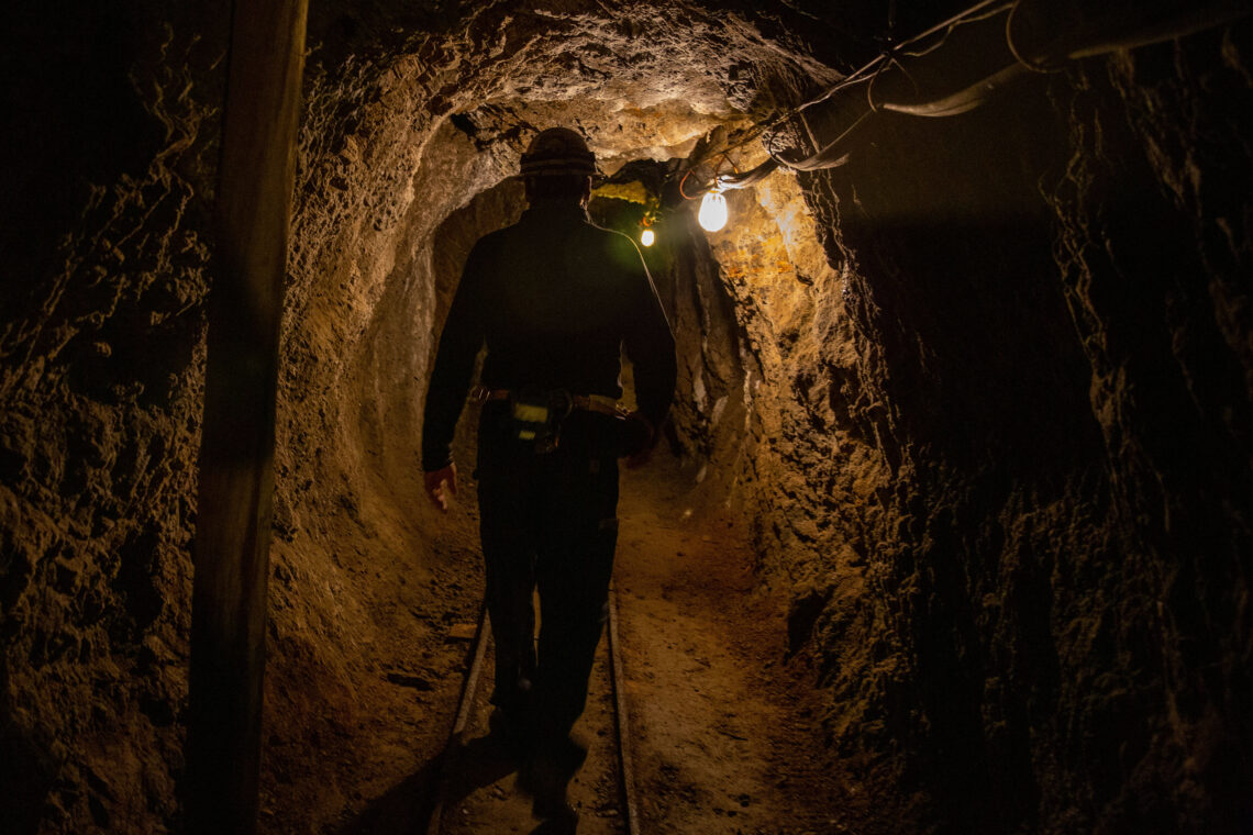Dark image of the back of a miner walking through a mine.
