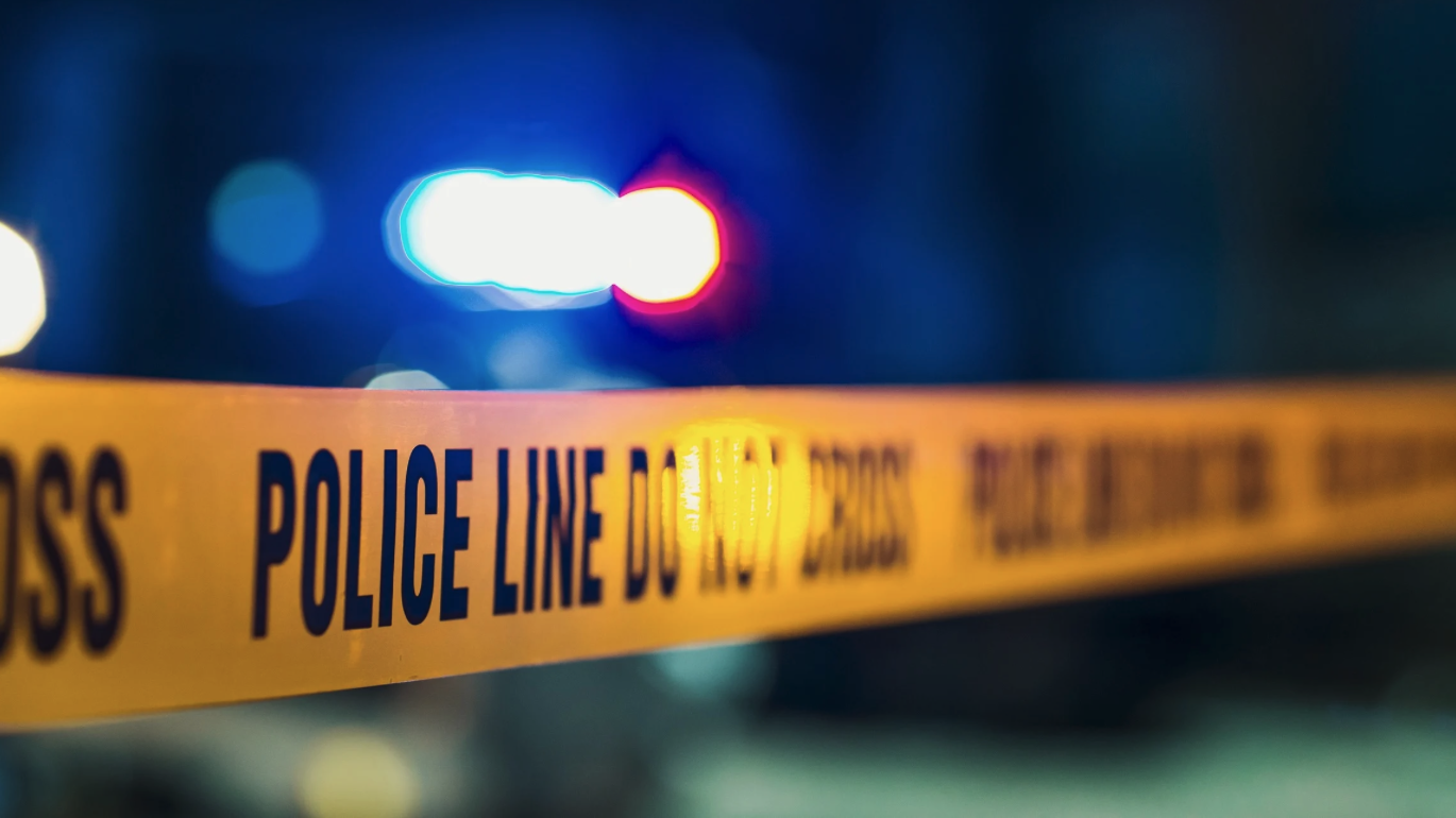 Image of police tape with the words POLICE LINE in all capital letters and the vague lights of a police car.