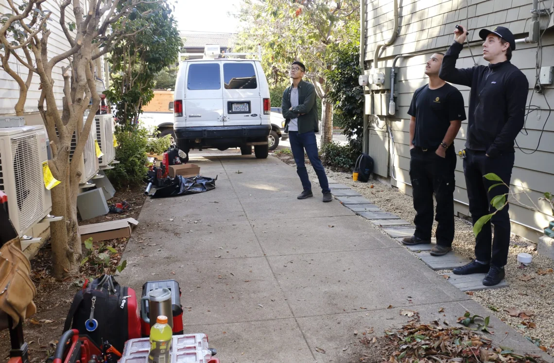 Three contractors stand in a driveway using a laser pointer to talk through installation strategy.
