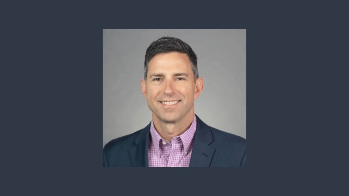 Man in pink collar shirt with a blue sports coat. He is framed with a grey border.