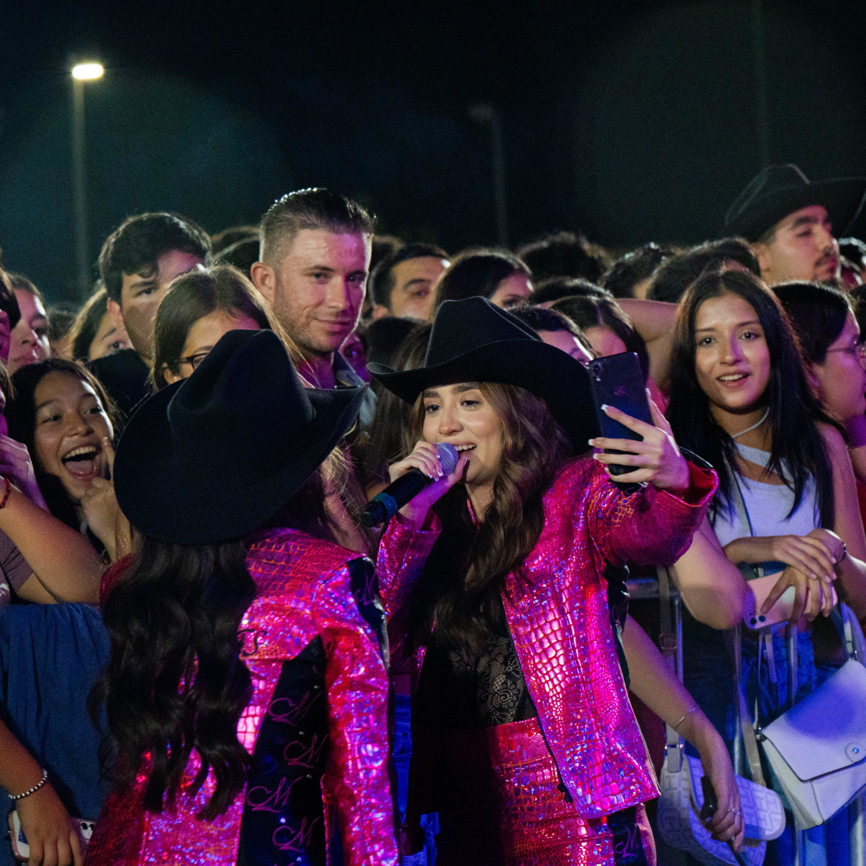 A photo of a crowd surrounding two singers in hot pink and glittery jackets.