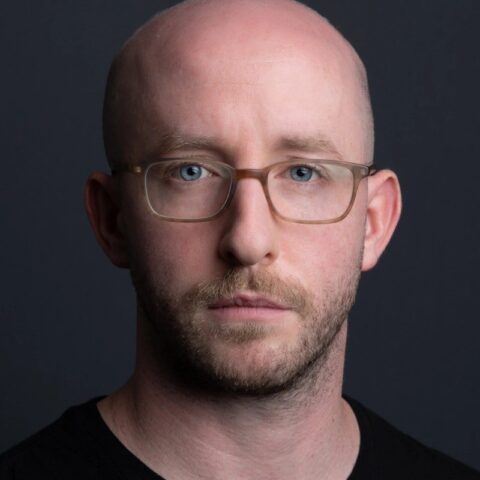 Brett_Murphy 2024 Closeup photo of a man with glasses and a light beard looking intently at the camera.