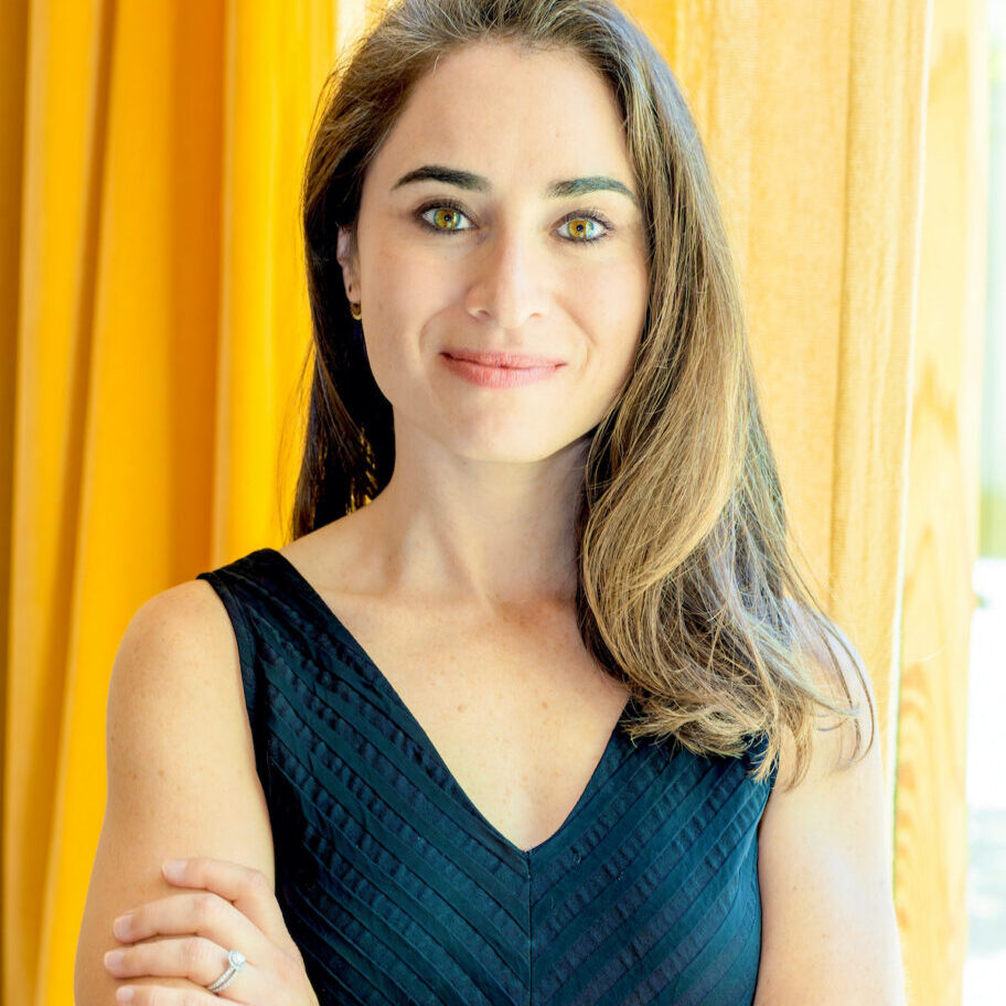 Hallie-Applebaum headshot of a young woman with long blond/brown hair wearing a blue dress, sleeveless.