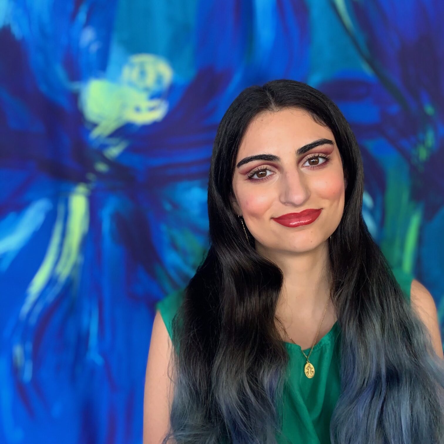Marissa Muller A woman with long, dark hair and a green top stands smiling in front of a blue abstract background.