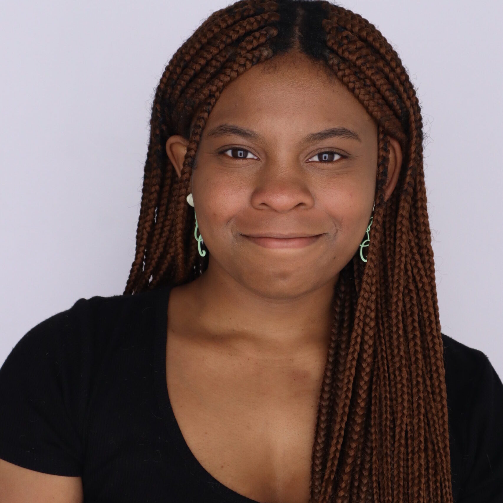 Nadia Lathan 2024 Photograph of journalist Nadia Lathan wearing a black short sleeve top and long braided hair smiling.