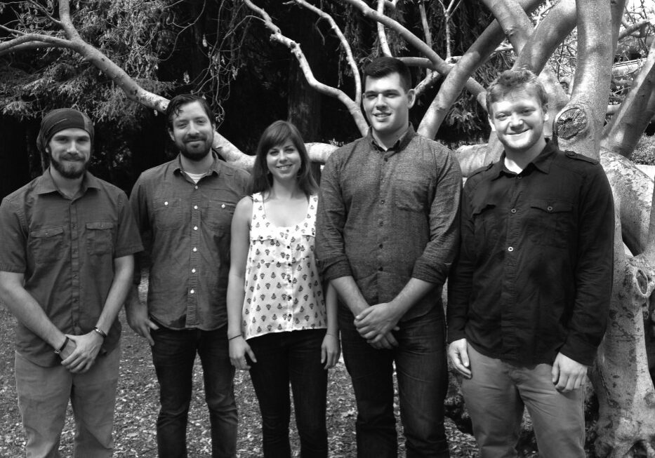 feltscholars3 A black and white photo shows five people standing outdoors in front of a large tree. Among them are two women and three men, all smiling and casually dressed. The branches of the tree create a detailed, natural backdrop, capturing a moment that could easily be featured in Berkeley Journalism.